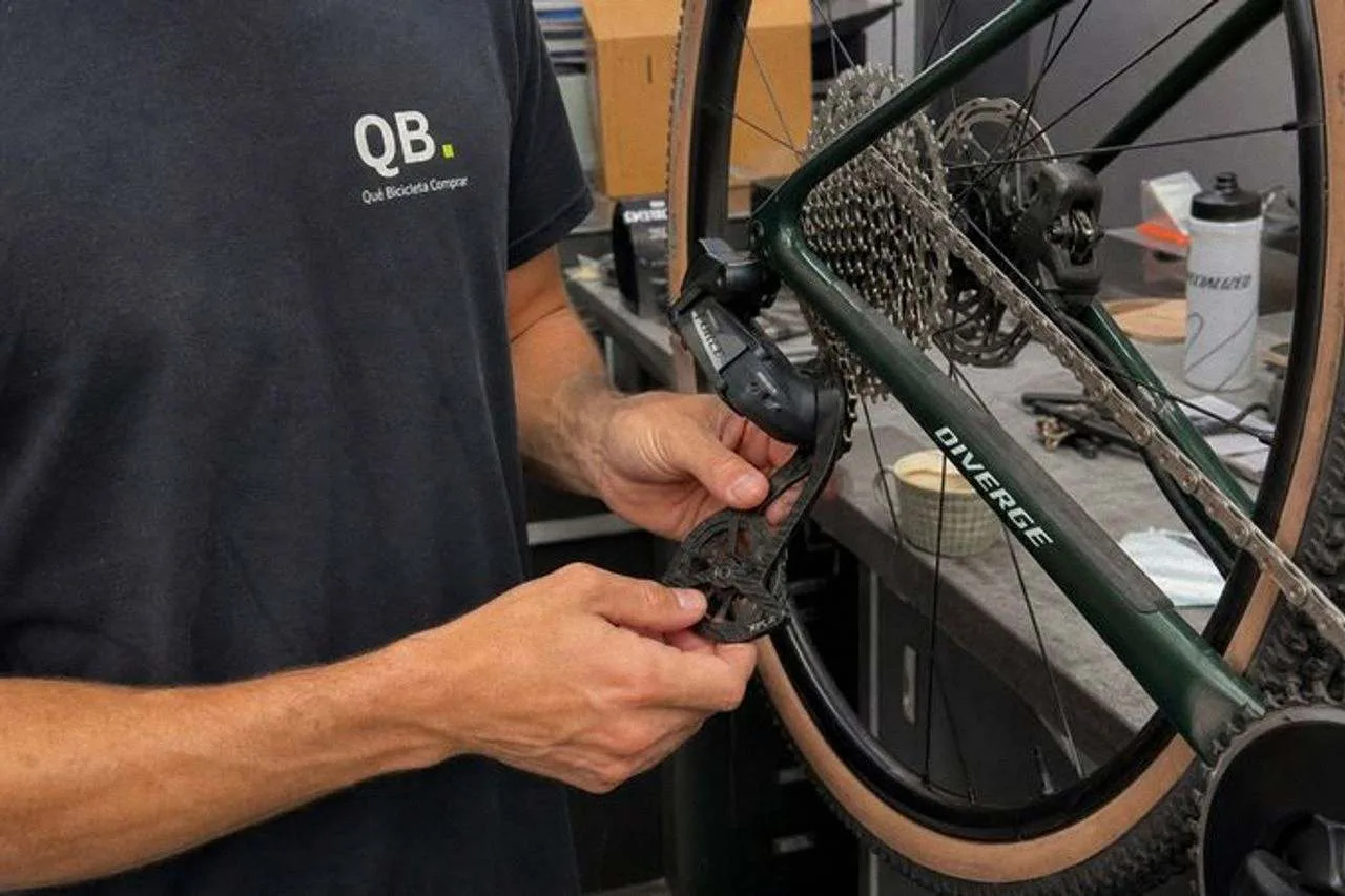 Dos manos giran el desviador trasero de una bicicleta de gravel sobre un caballete para leer el nombre del modelo impreso en la jaula.
