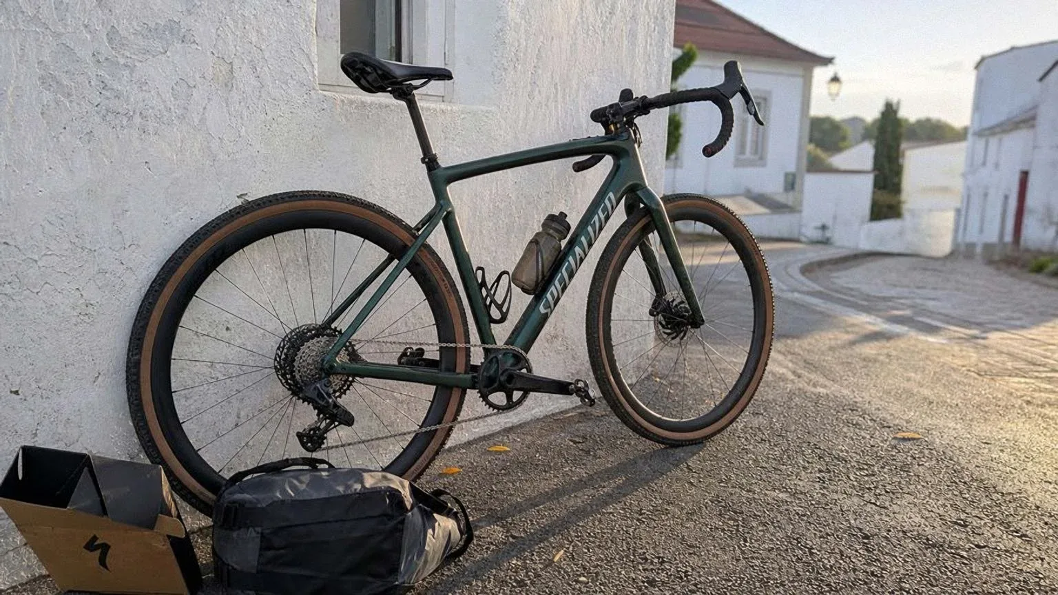 Bicicleta de gravel de carbono verde apoyada en una pared encalada al amanecer, con una bolsa de bikepacking a medio cargar junto a la rueda trasera.